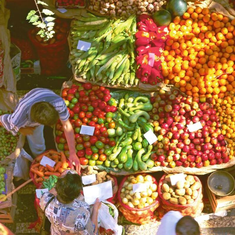 Menschen kaufen buntes Obst und Gemüse auf einem Marktstand aus der Vogelperspektive.