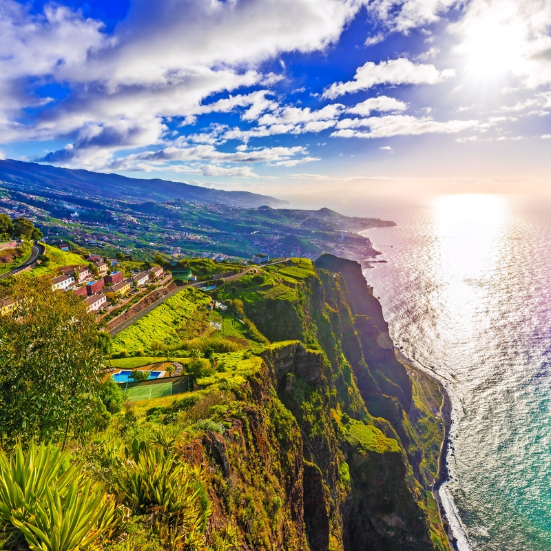 Küstenlandschaft mit steilen Klippen, grünem Vegetation und Blick auf das Meer bei Sonnenuntergang.