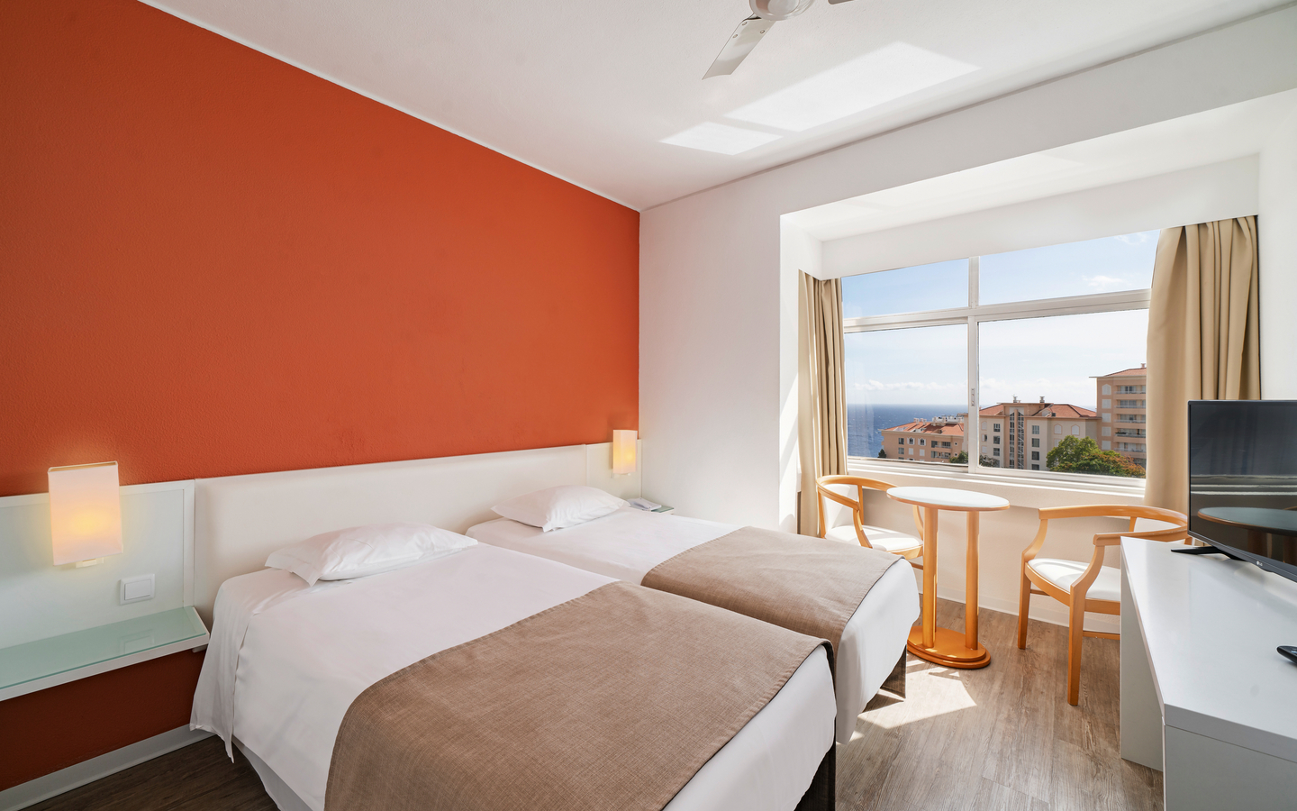 Helles Hotelzimmer mit zwei Betten, Fenster und Meerblick.