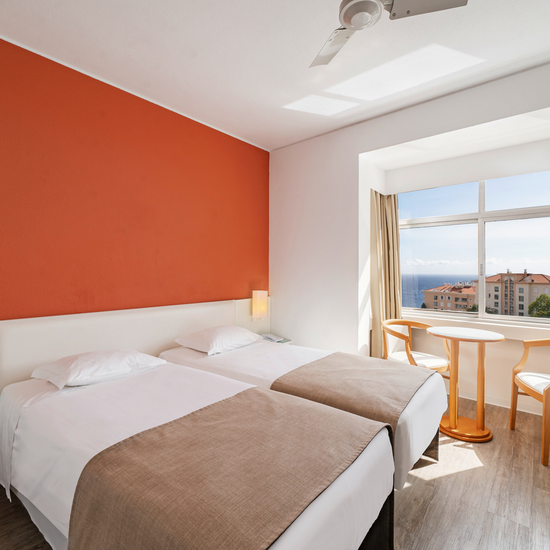 Helles Hotelzimmer mit zwei Betten, Fenster und Meerblick.