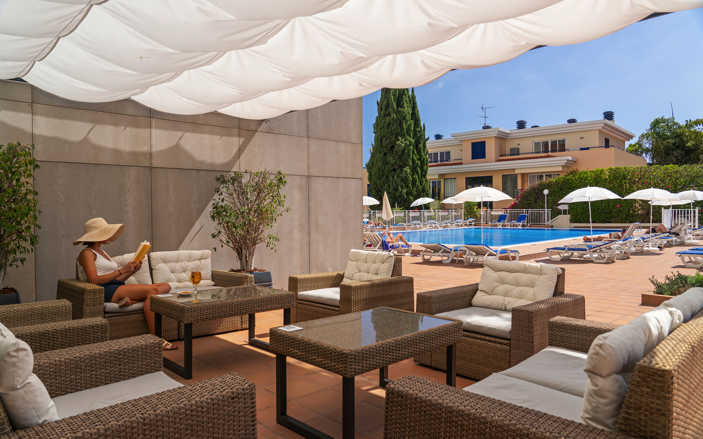 Außenterrasse des Hotels mit Pool und Sitzbereich unter weißen Sonnensegeln.