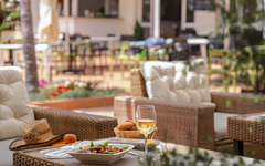 Tisch mit Essen und Weinglas auf einer sonnigen Terrasse im Hotelgarten.