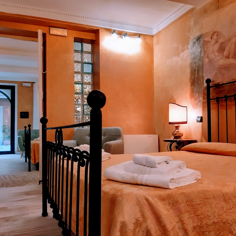 Hotelzimmer mit Doppelbett, Nachttischlampe und offenen Türen zum Flur und Hof.