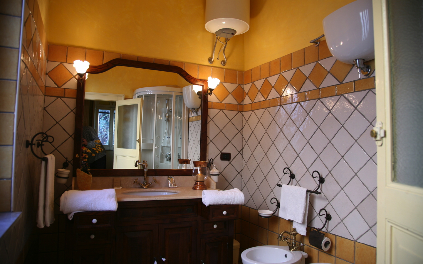 Hotelbad mit Waschbecken, Spiegel, Handtüchern und Fliesenwänden in warmen Farben.