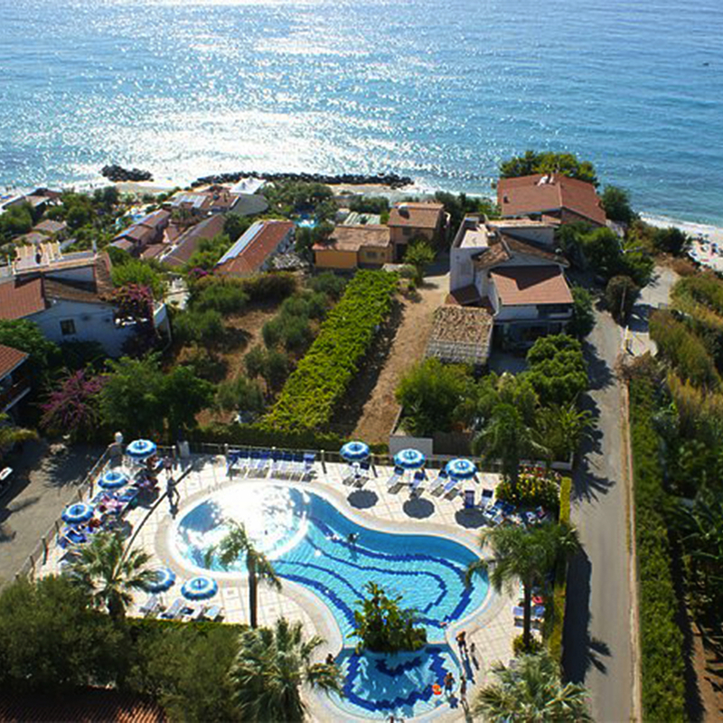 Luftaufnahme eines Resorts mit Pool, umgeben von Bäumen und Meerblick.