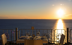 Tisch auf Terrasse mit Meeresblick und Sonnenuntergang im Hintergrund