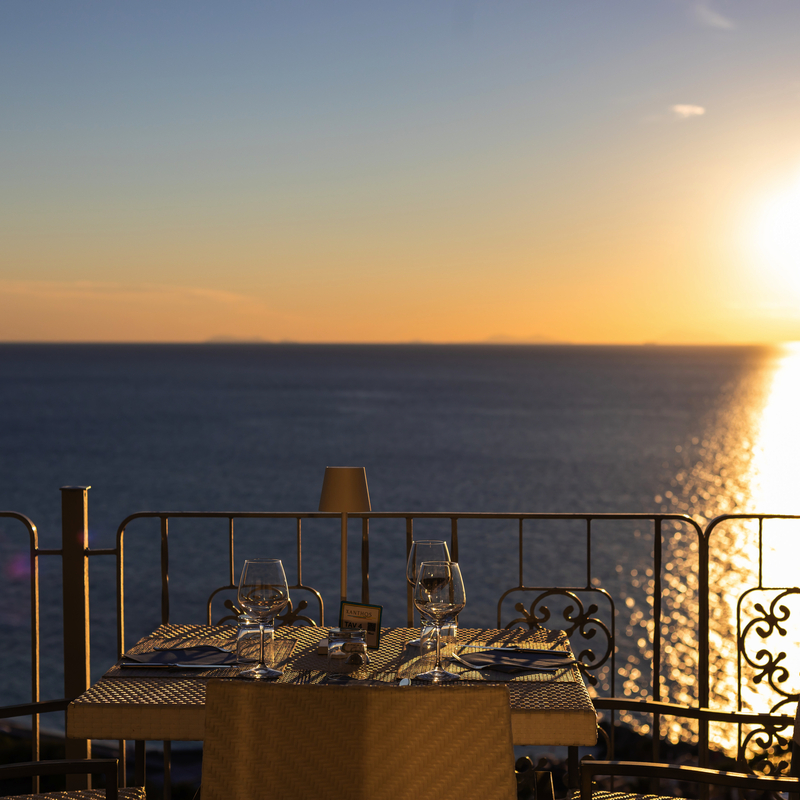 Tisch auf Terrasse mit Meeresblick und Sonnenuntergang im Hintergrund