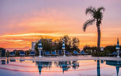 Poolbereich des Hotel Resort Tonicello bei Sonnenuntergang mit Palmen und Liegestühlen.