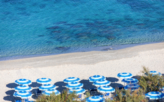 Strand mit blauen Sonnenschirmen und türkisfarbenem Wasser im Hotel Resort Tonicello.