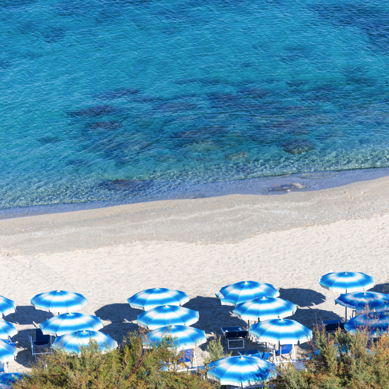 Strand mit blauen Sonnenschirmen und türkisfarbenem Wasser im Hotel Resort Tonicello.