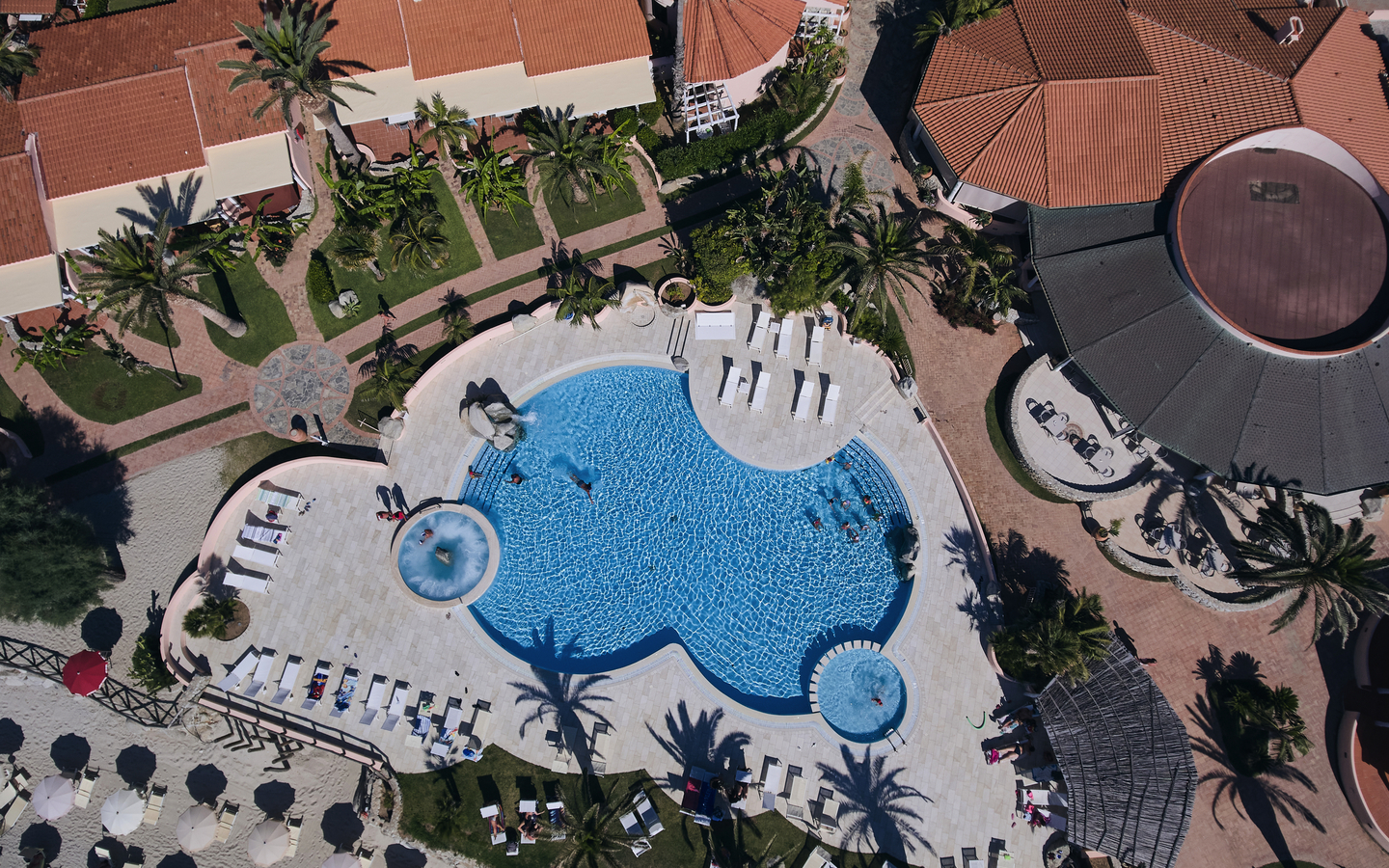 Luftaufnahme eines Hotelpools mit umliegenden Gebäuden und Palmen