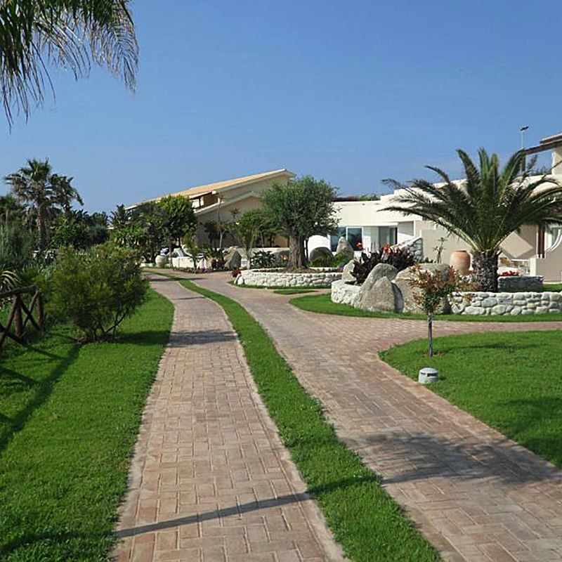 Gepflegter Gartenweg zum Hotelgebäude, umgeben von Palmen und Sträuchern.