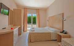 Helles Hotelzimmer mit Doppelbett und Blick auf Garten.