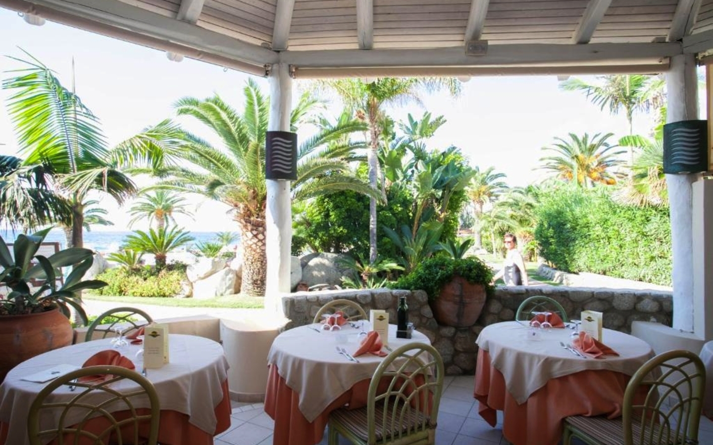 Gedeckte Tische auf einer Terrasse mit Meerblick und Palmen im Hintergrund