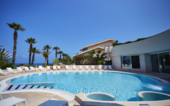 Hotelpool mit Liegestühlen und Palmen im Hintergrund.