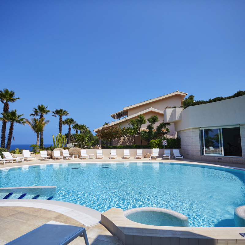 Hotelpool mit Liegestühlen und Palmen im Hintergrund.