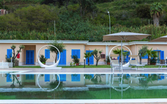 Pool mit modernen Liegen und blauen Türen im Hintergrund vor grüner Landschaft.