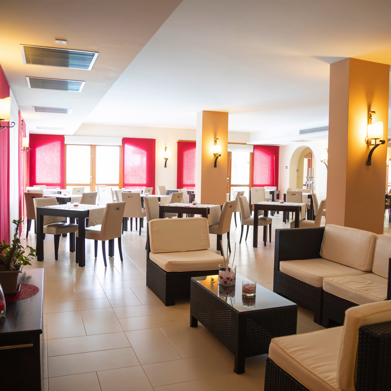 Helles Hotel-Restaurant mit modernen Möbeln und rotem Fensterakzent.