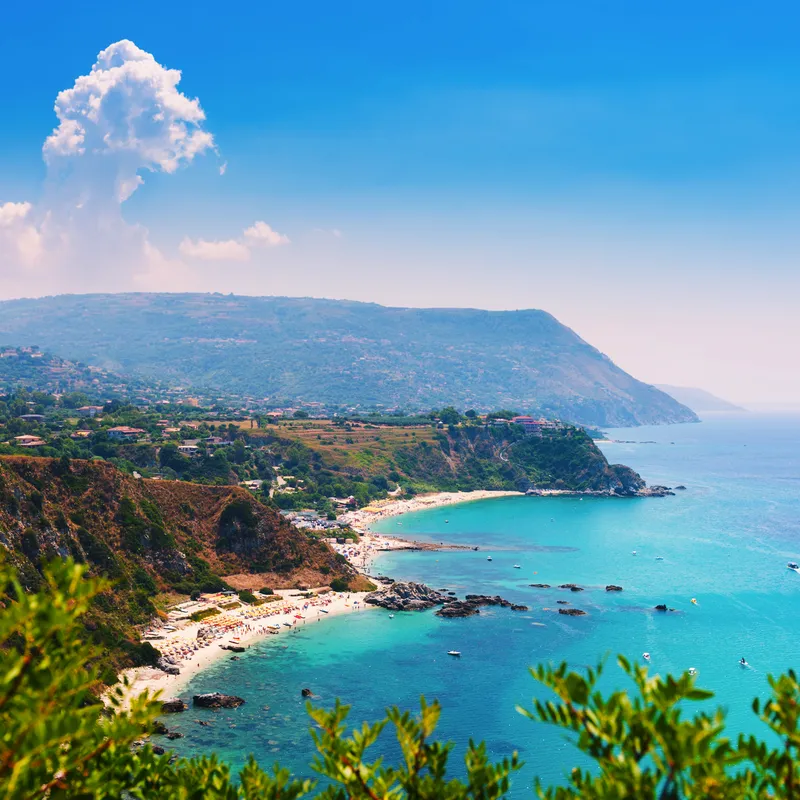 Küste mit klarem, türkisfarbenem Wasser und bewaldeten Klippen unter blauem Himmel.