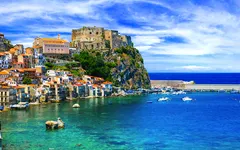 Küstenstadt mit farbenfrohen Gebäuden und einer Burg auf einem Hügel am Meer.