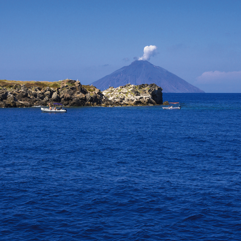 Blick auf blauen Ozean mit Booten und Vulkan am Horizont.