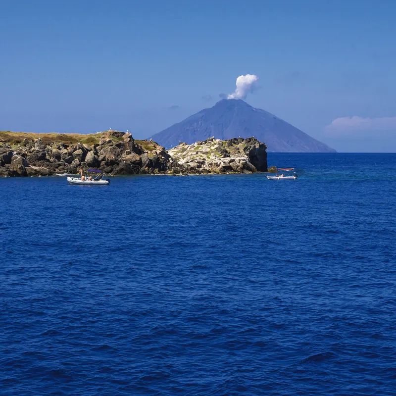 Blick auf blauen Ozean mit Booten und Vulkan am Horizont.