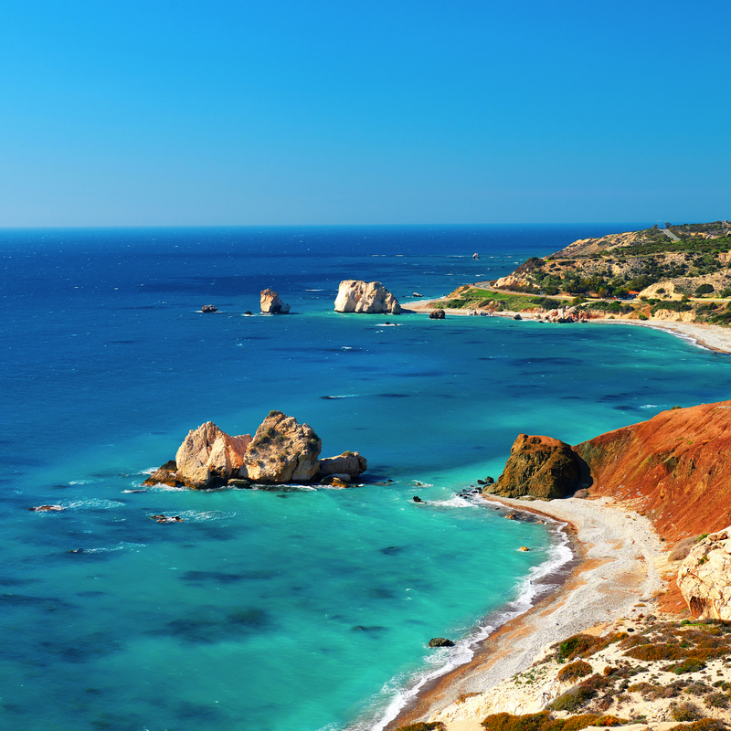 Küstenlandschaft mit blauem Wasser und Felsen unter blauem Himmel.