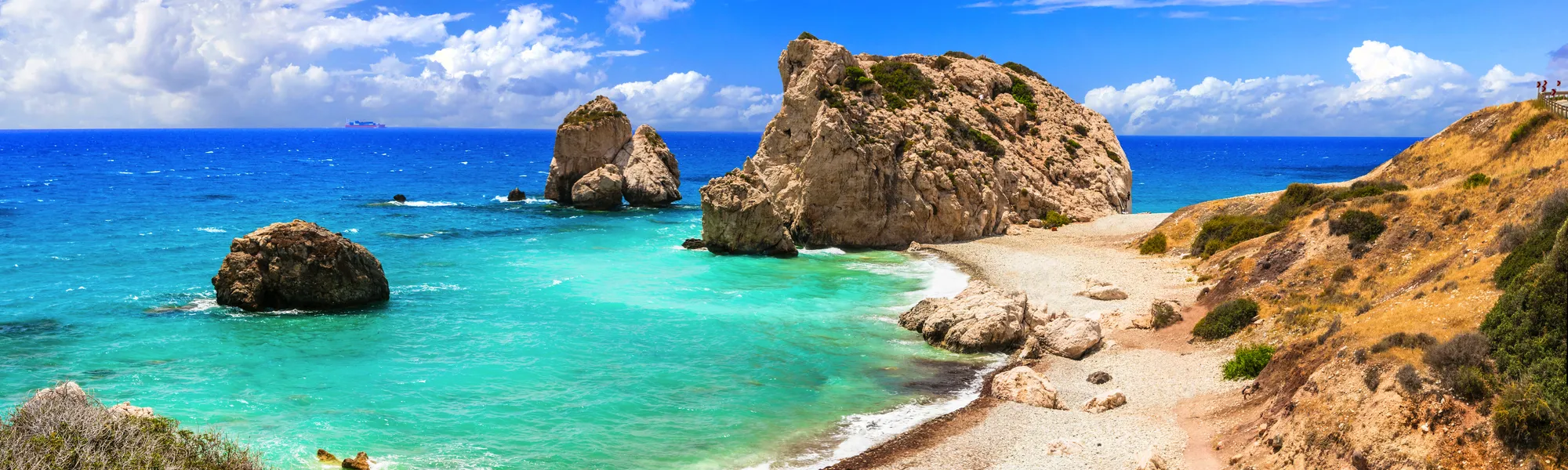 Küstenlandschaft mit Felsen und türkisblauem Meer unter blauem Himmel.