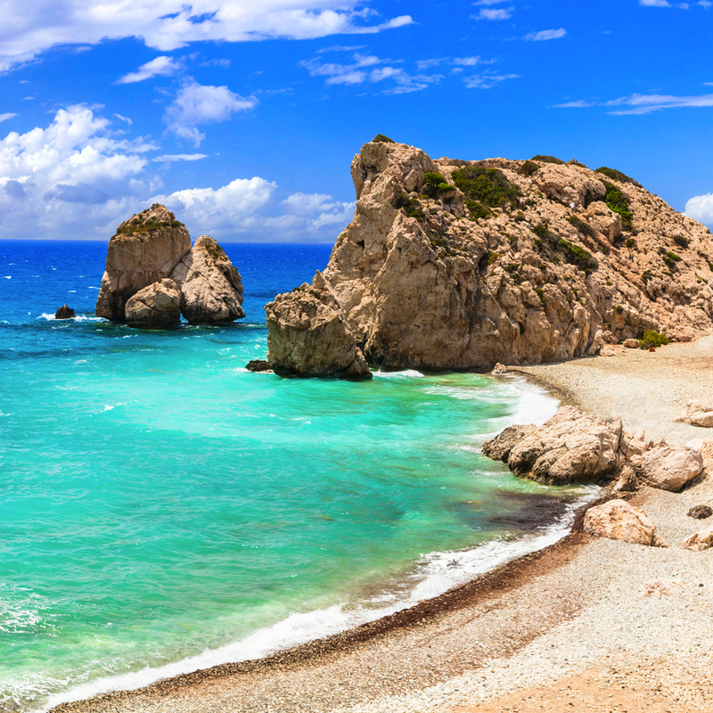 Küstenlandschaft mit Felsen und türkisblauem Meer unter blauem Himmel.