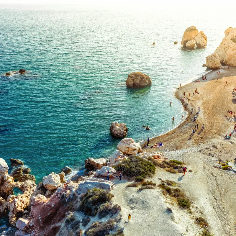 Küste mit Felsen und klarem Meerwasser, Menschen genießen den Strand.