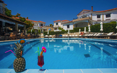 Hotelpool mit Getränken und Liegestühlen, umgeben von weißen Gebäuden.