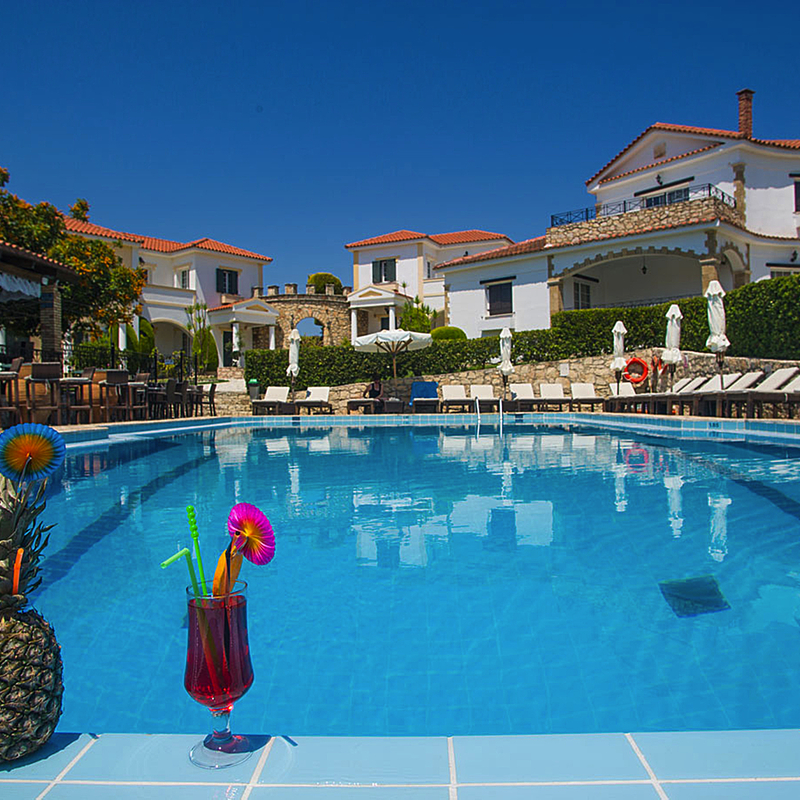 Hotelpool mit Getränken und Liegestühlen, umgeben von weißen Gebäuden.
