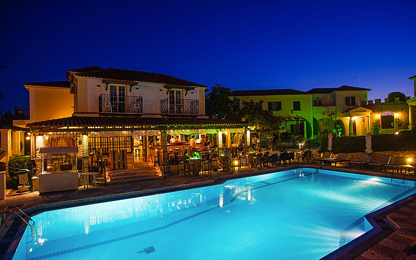 Beleuchteter Hotelpool bei Nacht vor einem Gebäude in Griechenland.