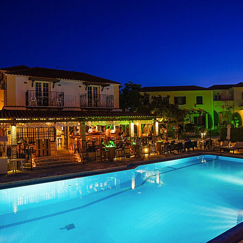 Beleuchteter Hotelpool bei Nacht vor einem Gebäude in Griechenland.