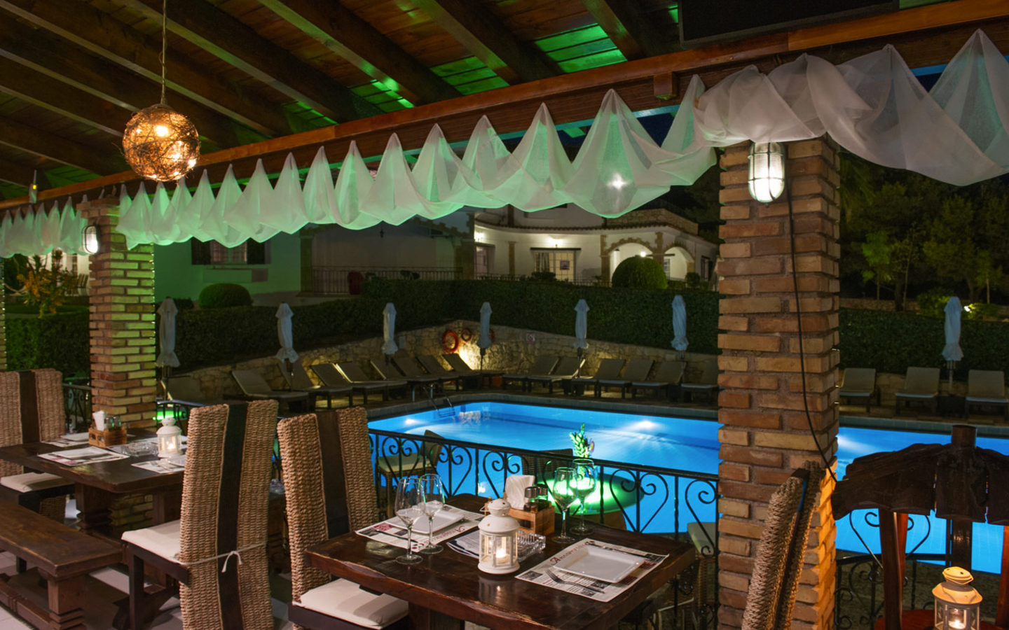 Restaurantterrasse mit Blick auf beleuchteten Pool in einer Hotelanlage bei Nacht.
