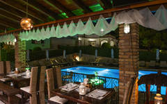 Restaurantterrasse mit Blick auf beleuchteten Pool in einer Hotelanlage bei Nacht.