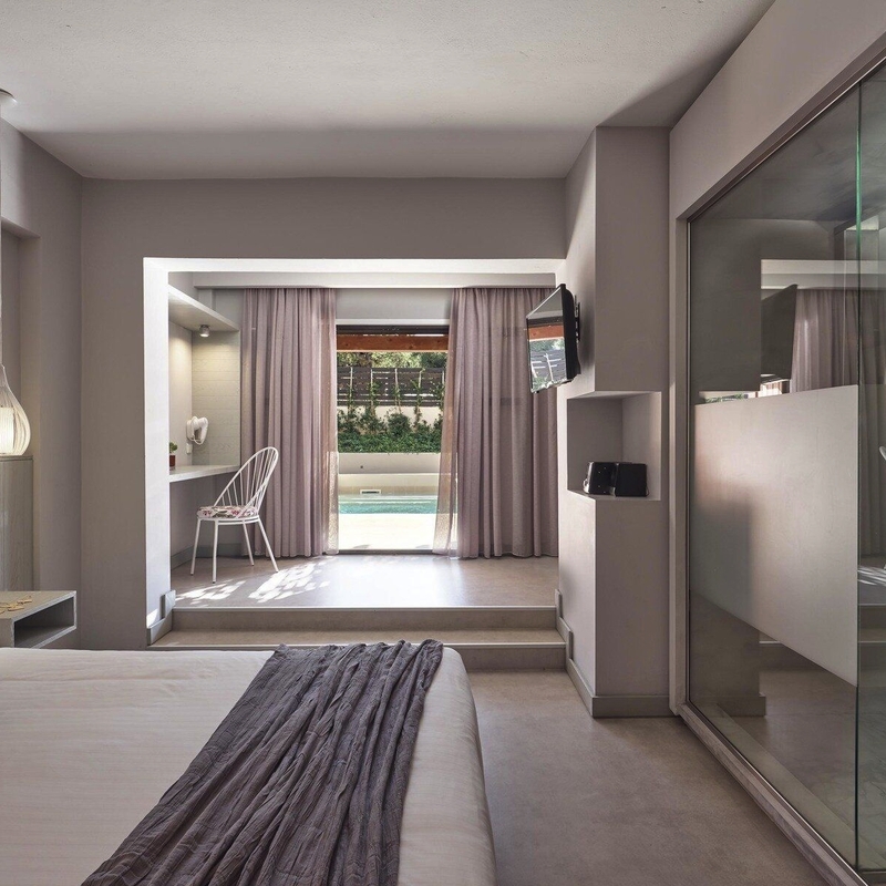 Modernes Hotelzimmer mit Bett, Glaswand und Blick auf Pool.