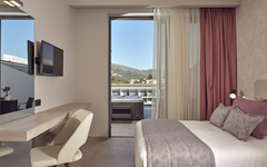 Modernes Hotelzimmer mit Doppelbett, Schreibtisch, TV und Blick auf die Terrasse.