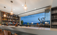 Moderne Hotelbar mit großen Fenstern, stilvoller Einrichtung und Ausblick auf das Meer.
