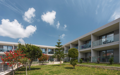 Hotelgebäude mit Balkonen und Garten im Vordergrund unter blauem Himmel.