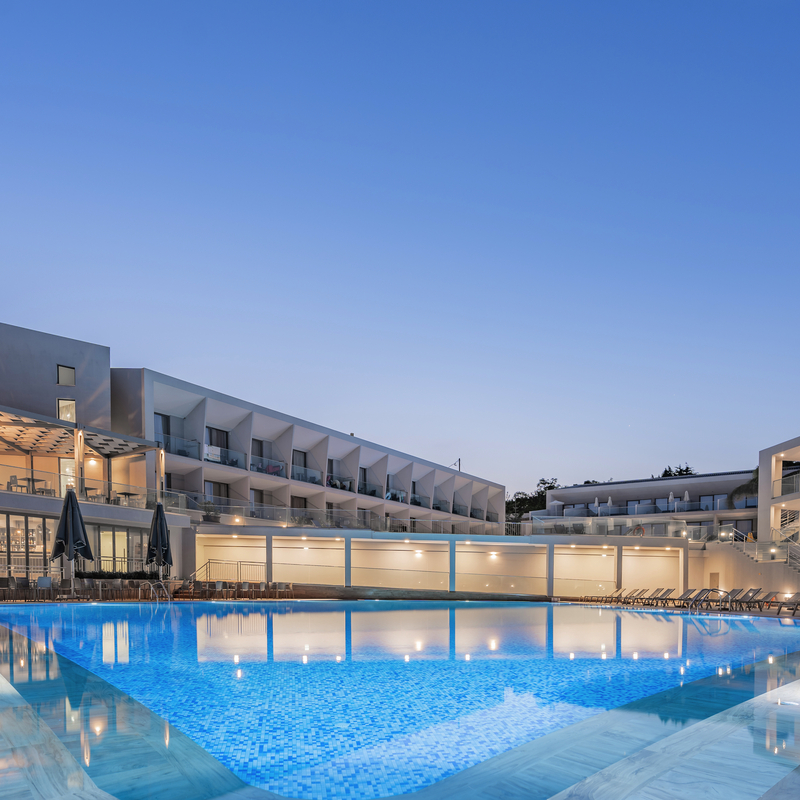 Hotelpool und Gebäude des Zante Sun bei Dämmerung, Palmen im Hintergrund.