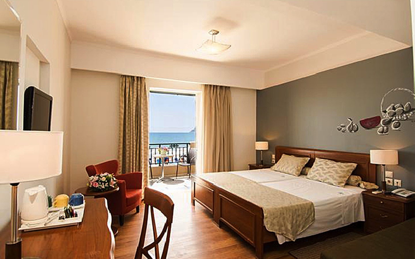 Helles Hotelzimmer mit Doppelbett, Schreibtisch und Balkon mit Meerblick.