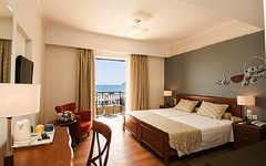 Helles Hotelzimmer mit Doppelbett, Schreibtisch und Balkon mit Meerblick.