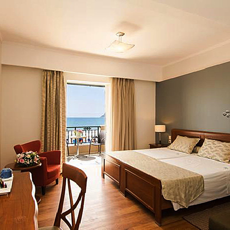 Helles Hotelzimmer mit Doppelbett, Schreibtisch und Balkon mit Meerblick.