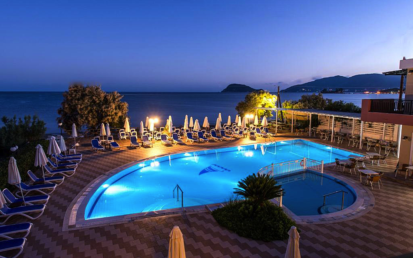Hotelpool bei Abenddämmerung mit Meerblick und Liegestühlen in Griechenland.