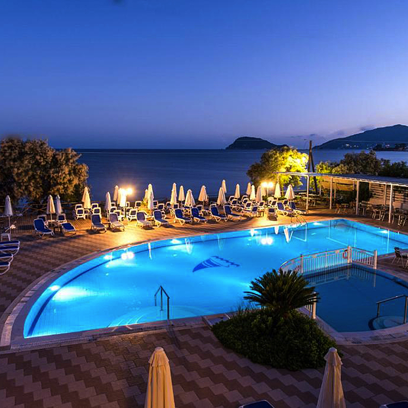 Hotelpool bei Abenddämmerung mit Meerblick und Liegestühlen in Griechenland.