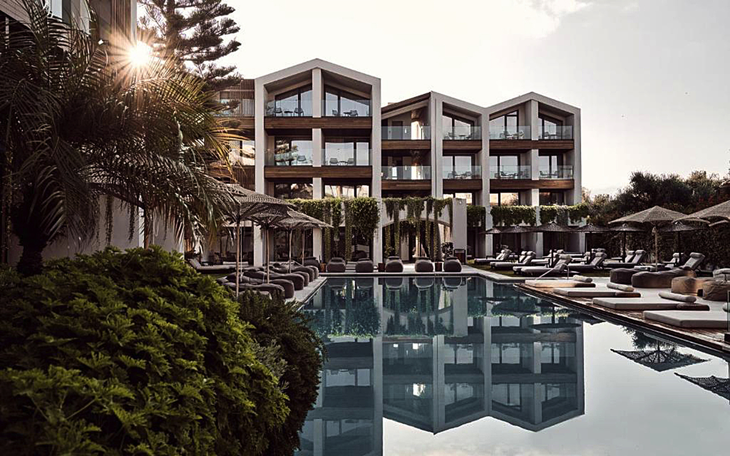 Modernes Hotelgebäude mit Pool und Sonnenliegen bei Sonnenuntergang.
