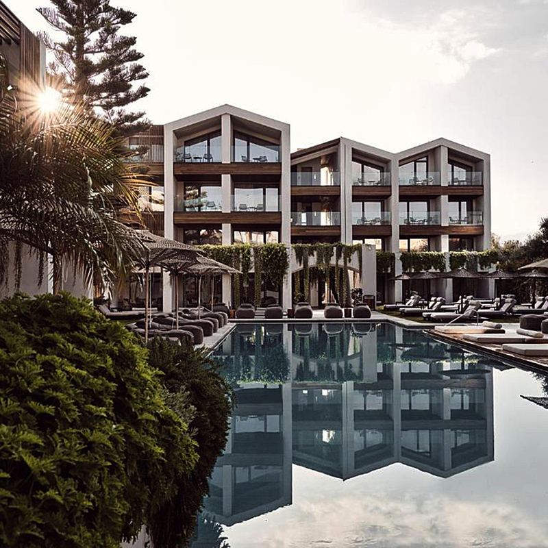 Modernes Hotelgebäude mit Pool und Sonnenliegen bei Sonnenuntergang.