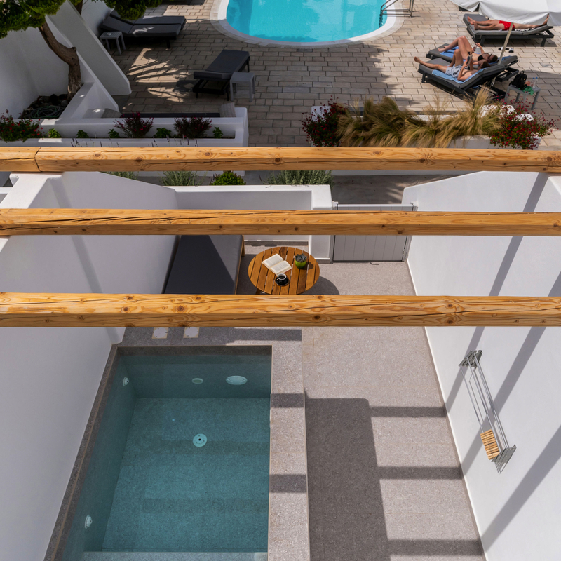 Blick von oben auf einen kleinen Pool und eine Terrasse mit Sonnenliegen in Santorin.