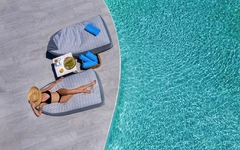 Frau entspannt sich auf Liege am Pool, sonniger Tag, türkisfarbenes Wasser.